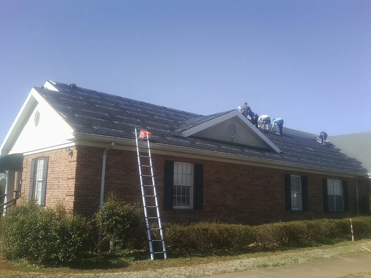 Crew tearing shingles off a brick ranch roof with a ladder set — Emergency Roof Repair work by our crew in Eau Claire