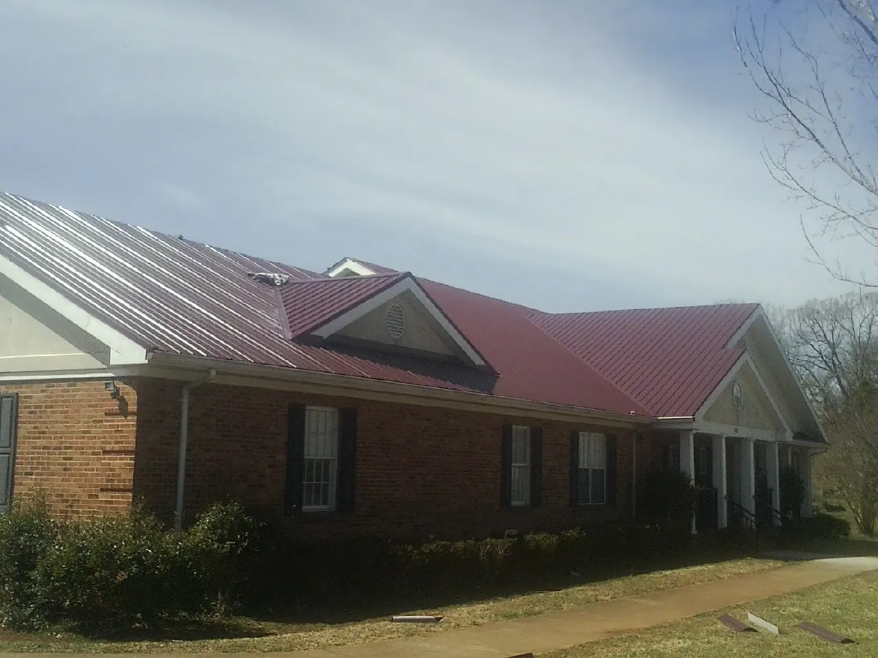 Red metal roof with gabled entries on a long brick building, from a Hail Damage Roof Repair job in Eau Claire