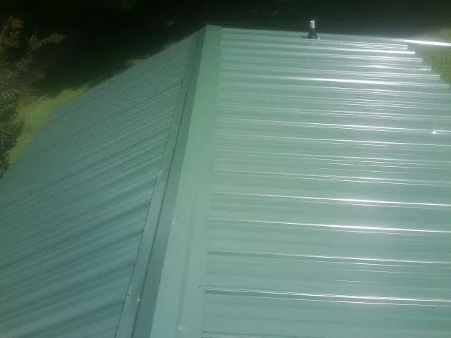 New green metal panels meeting at the ridge of a roof — Flat Roof Repair work by our crew in Eau Claire