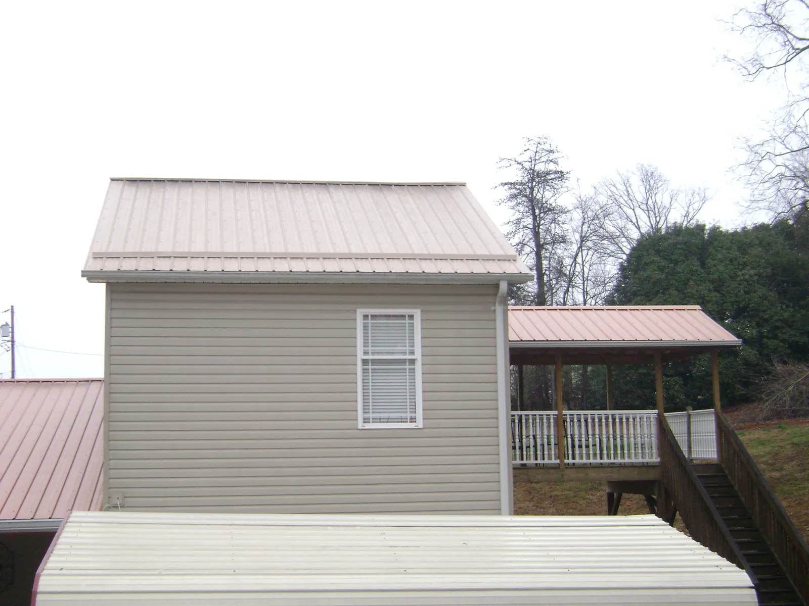 Tan metal roofs on a two story addition and attached porch, from a Roof Replacement job in Eau Claire