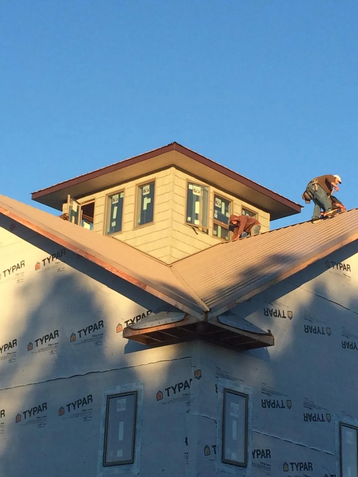 Roofers working around a rooftop cupola on a new metal roof at sunset — Roof Waterproofing in Eau Claire by Roofing Brothers